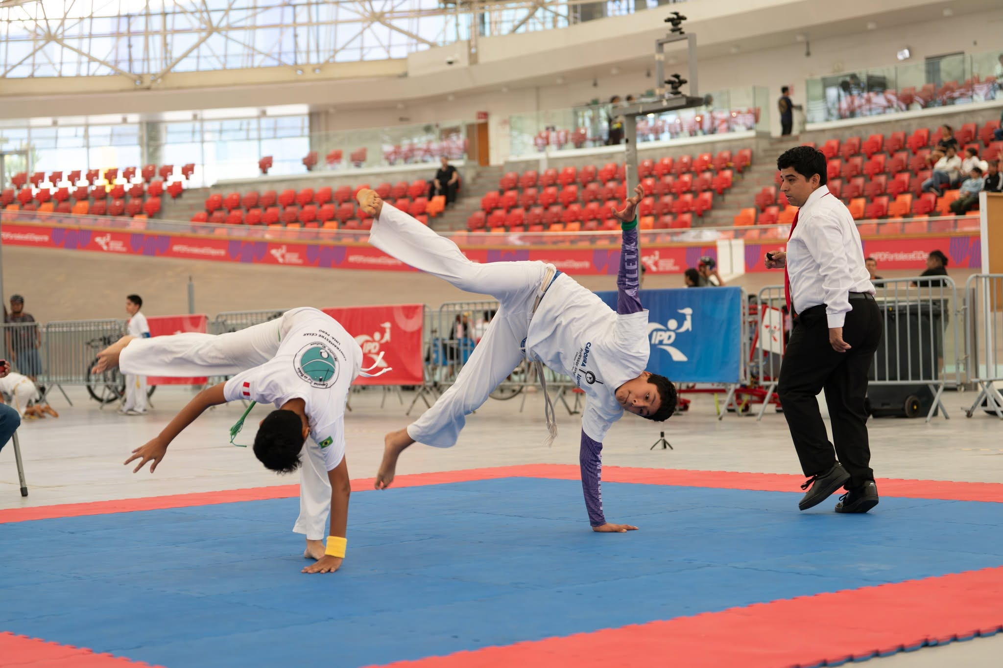 Dos deportistas de capoeira en competencia con supervisión arbitral